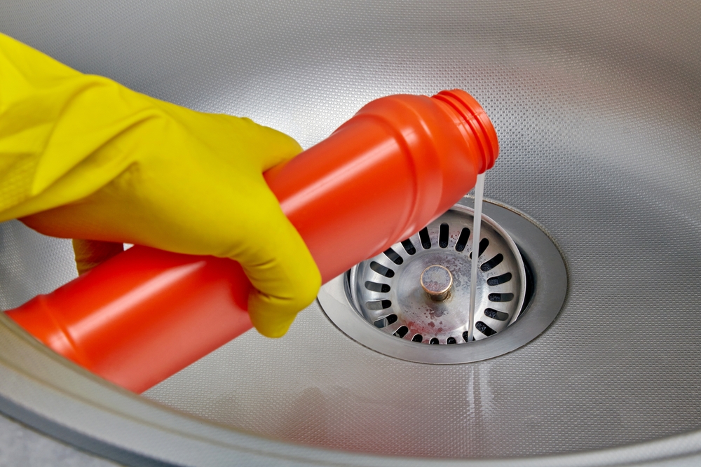 Person pouring liquid drain cleaner down kitchen sink drain